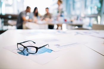 glasses sitting on papers with a business meeting in background